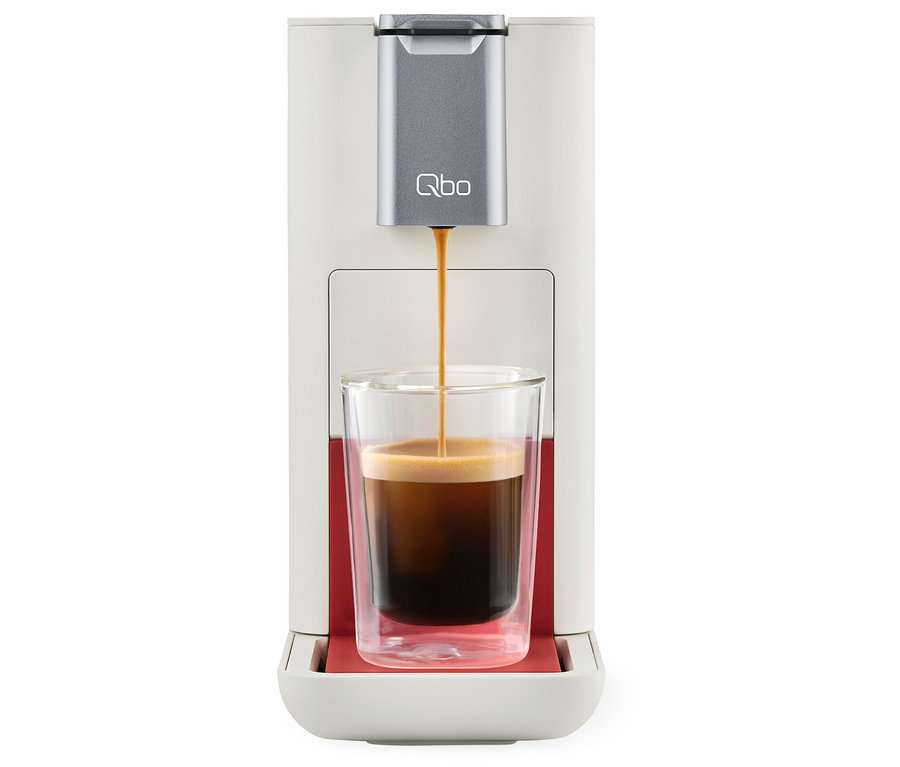 Kaffee läuft aus einer Qbo ESSENTIAL Bright Coral Kaffeemaschine in ein Glas.