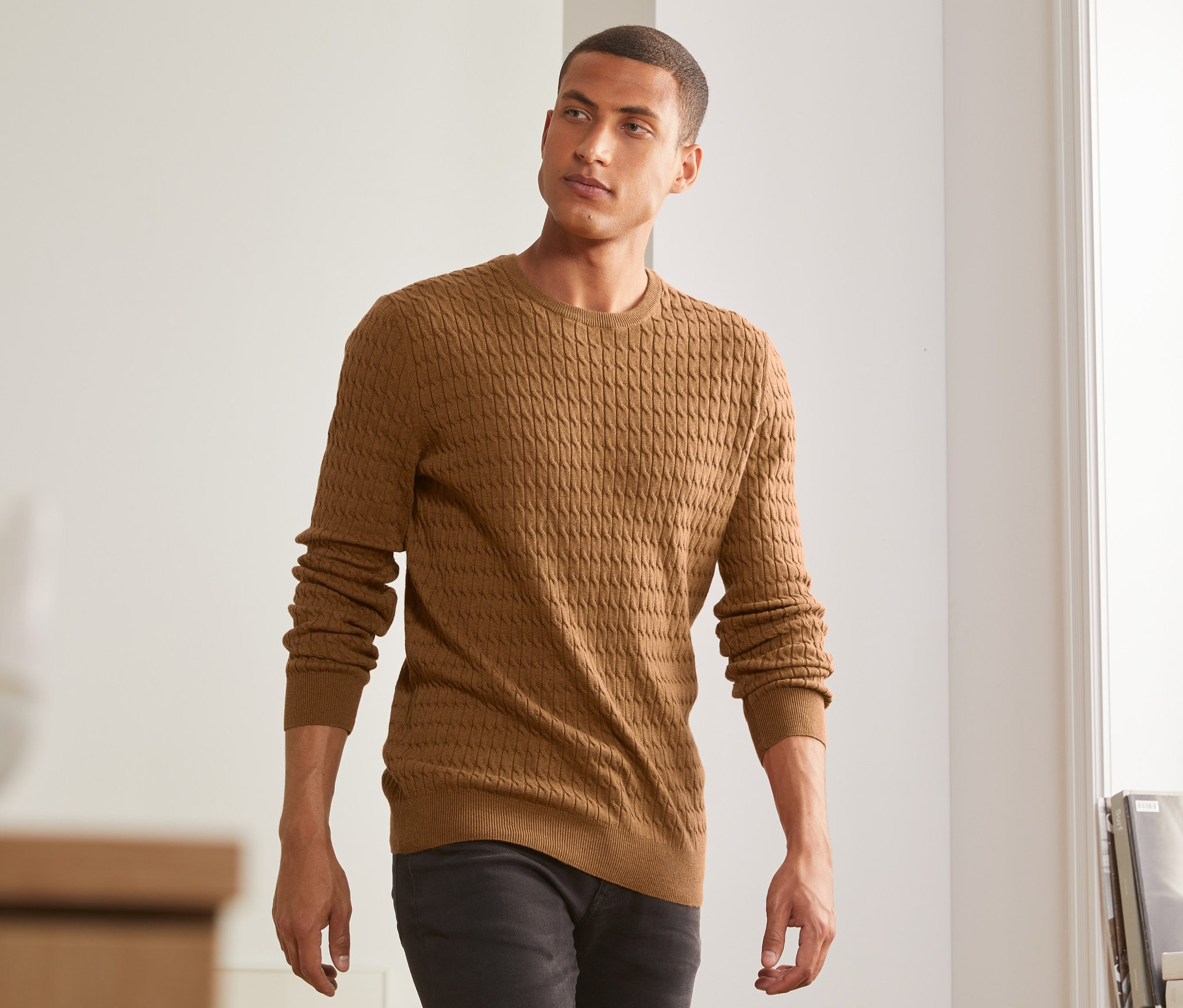 Mann trägt einen senfgelb melierten Strickpullover.