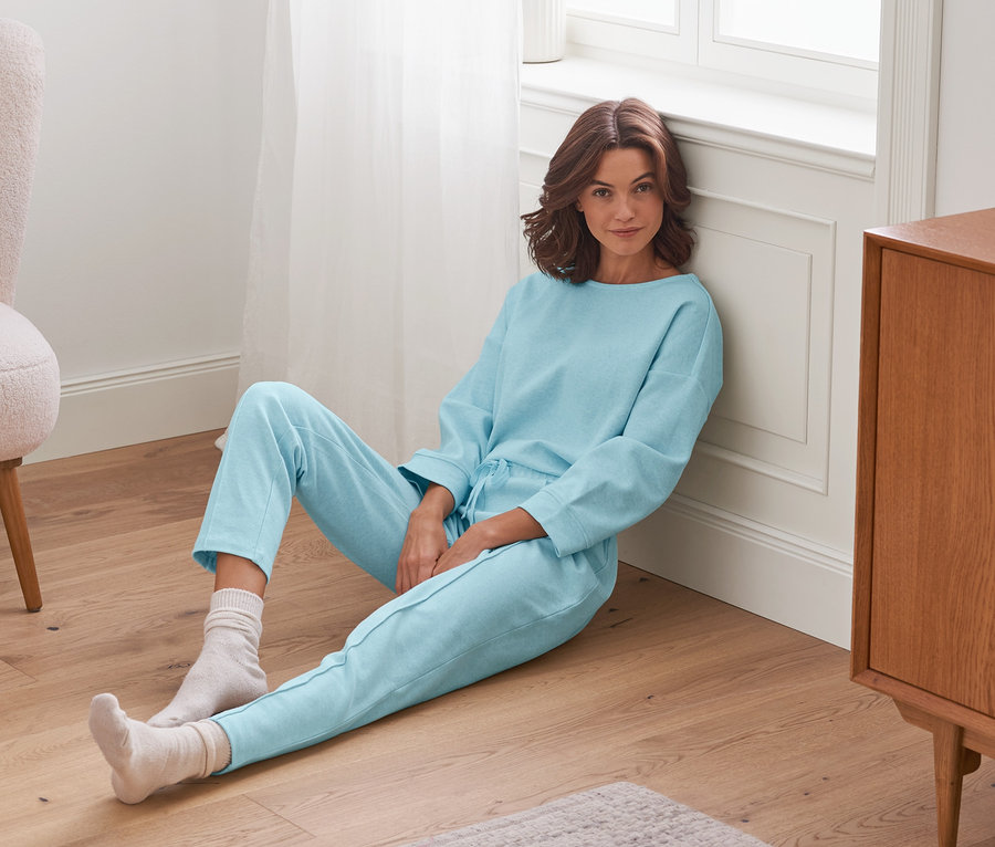 Frau sitzt mit einer Loungewear-Hose und Socken auf dem Boden.