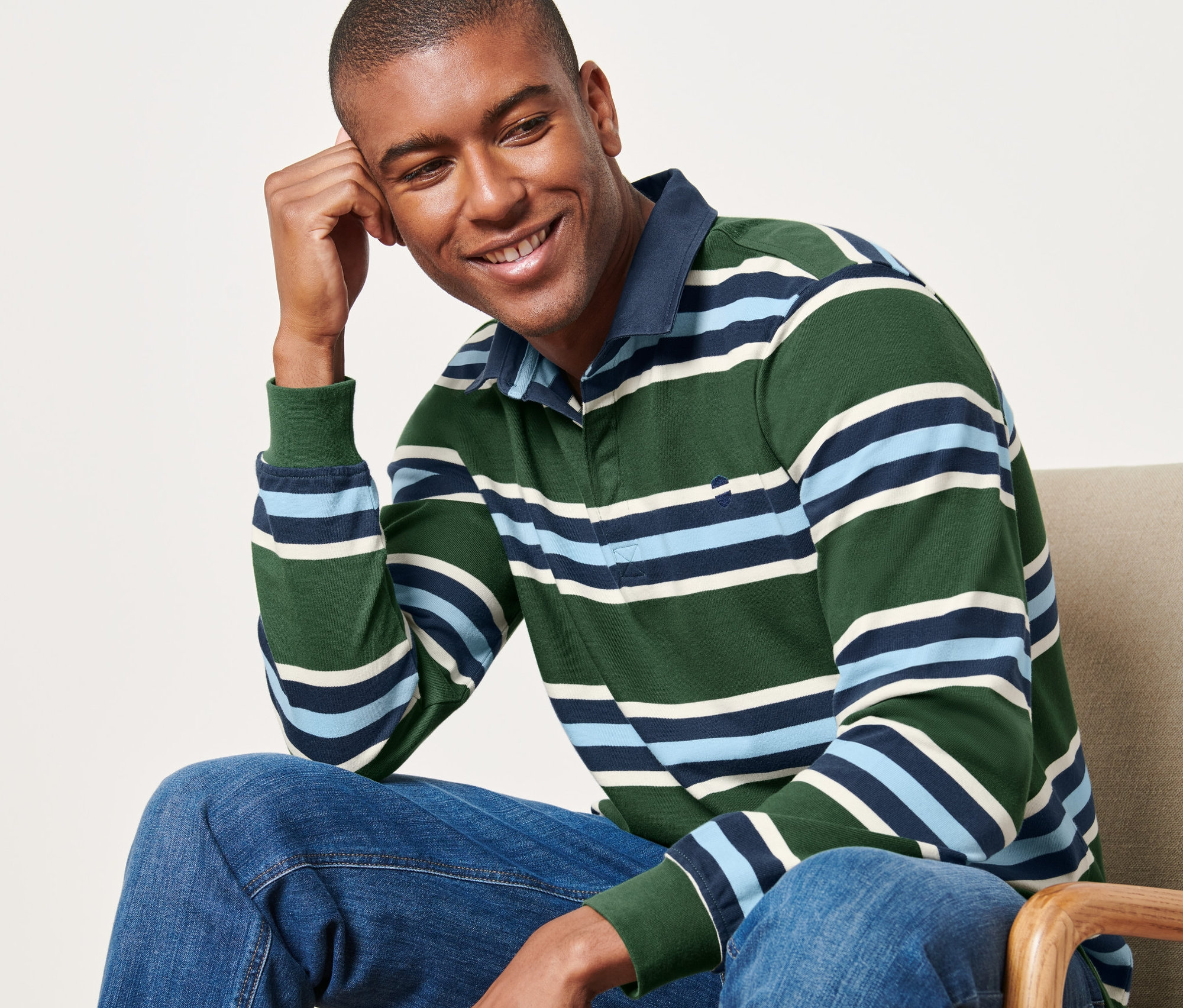 Mann sitzt auf einem Stuhl und trägt ein Langarm-Poloshirt.