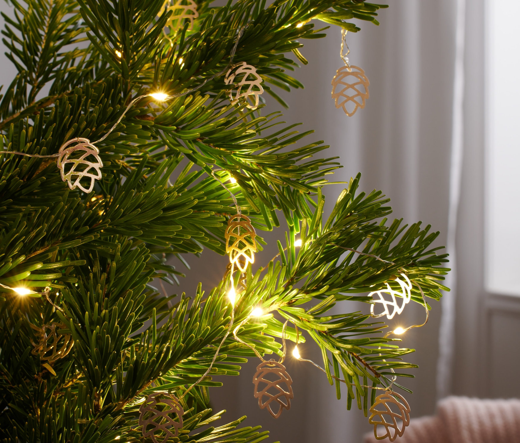 LED-Microlichterkette mit Tannenzapfen auf einem grünen Baum.