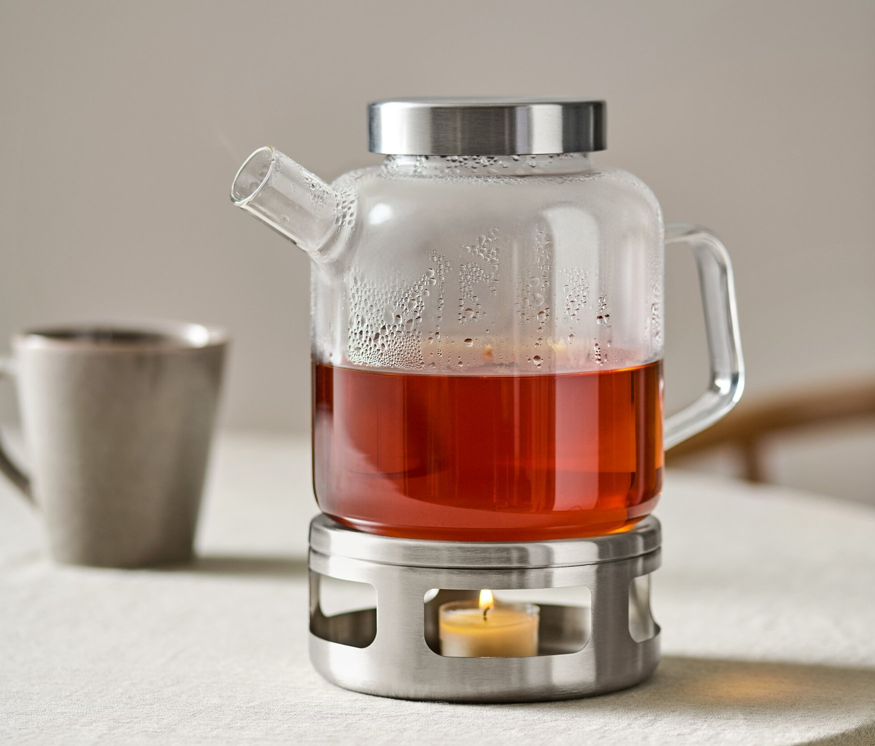 Glastopf mit Tee steht auf einem Stövchen mit einer brennenden Kerze.