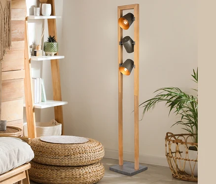 Innenraum mit hölzernem Leiterregal, Sitzpoufs aus Korbweide und Trio Stehleuchte "Bell" mit drei Lampen.