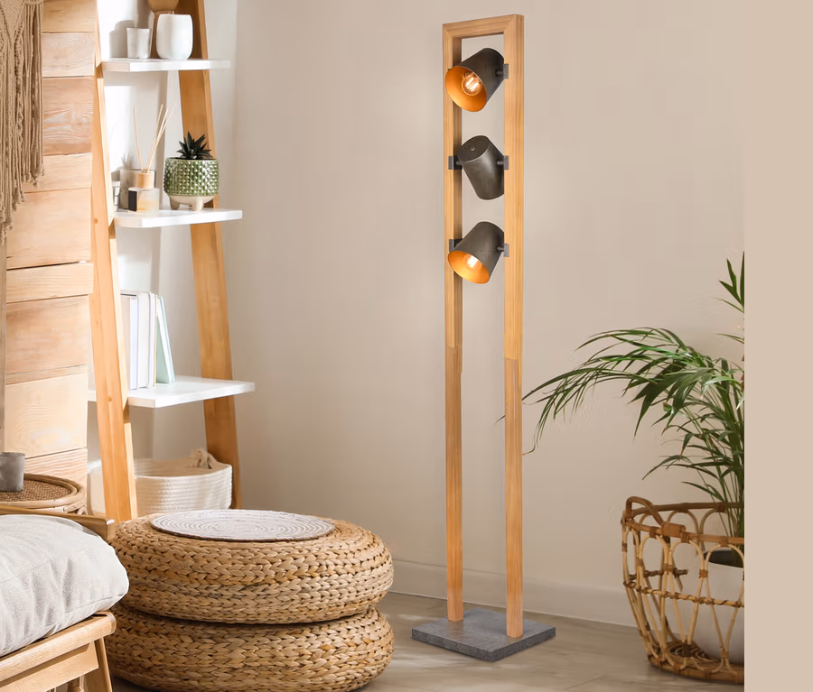Innenraum mit hölzernem Leiterregal, Sitzpoufs aus Korbweide und Trio Stehleuchte "Bell" mit drei Lampen.