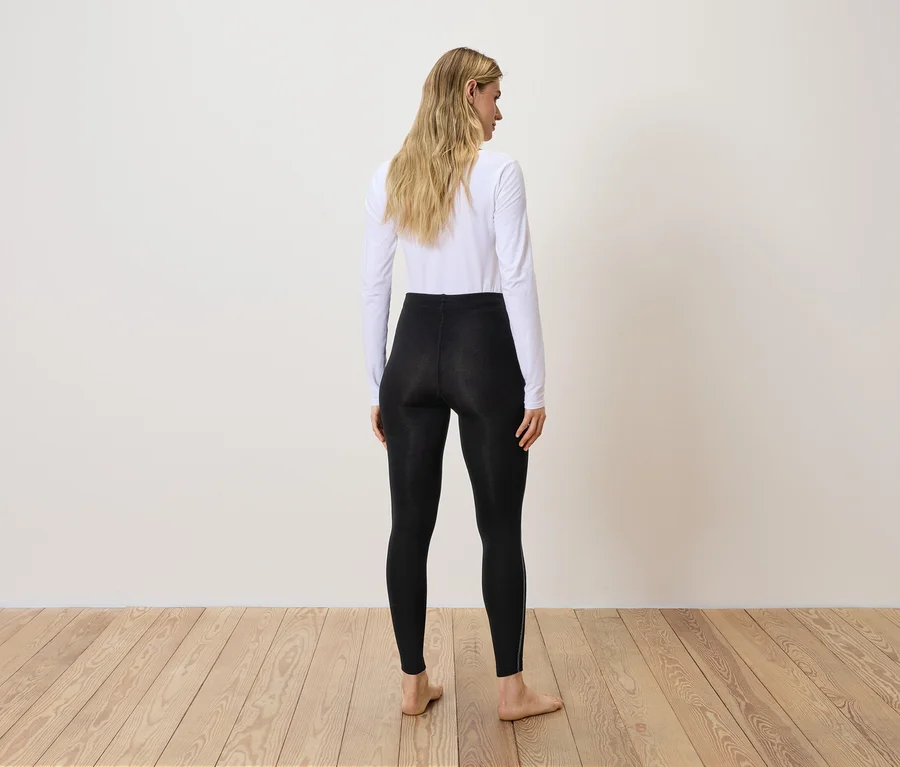 Rückansicht einer Frau mit blonden Haaren in schwarzen Leggings und weißem Oberteil.