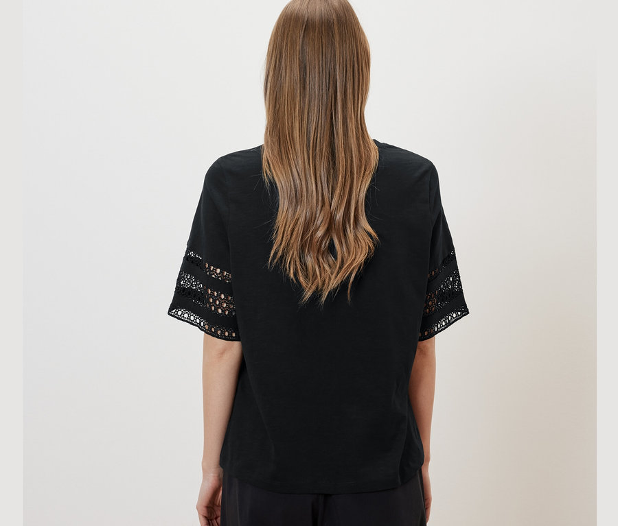 Rückansicht einer Frau mit braunen Haaren, die ein schwarzes Shirt mit Stickerei und eine schwarze Hose trägt.
