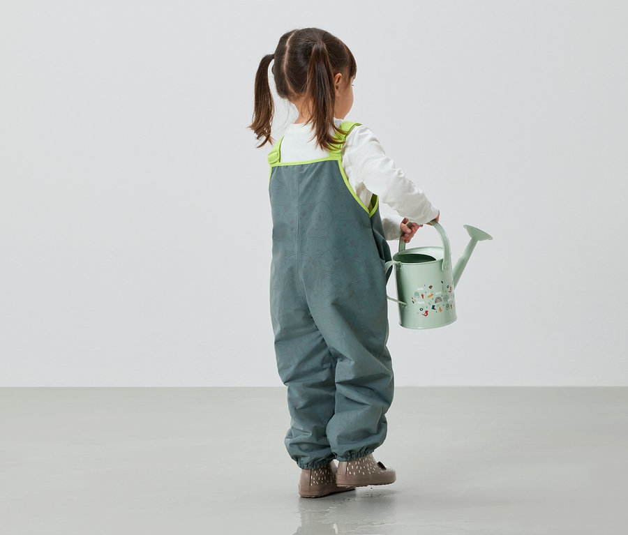 Mädchen in grauer Hose hält grüne Gießkanne in der Hand.