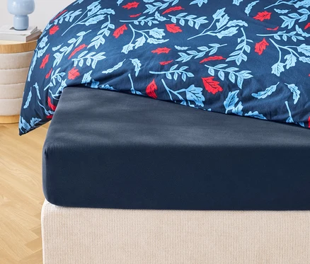 Detailansicht eines dunkelblauen Spannbetttuchs und einer gemusterten Bettdecke mit Blumenmuster.