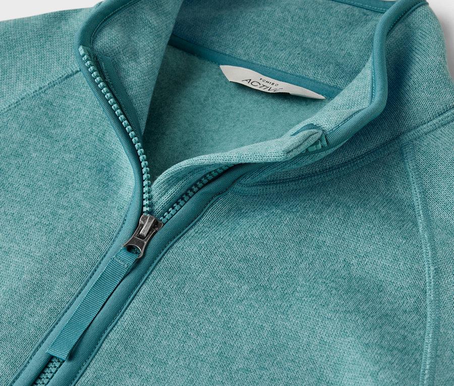 Detailaufnahme einer blaugrünen Fleecejacke mit Reißverschluss.