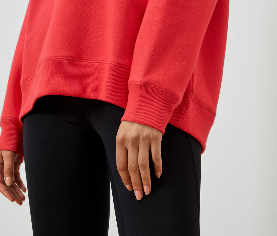 Detailaufnahme einer Frau, die einen roten Pullover und schwarze Leggings trägt.