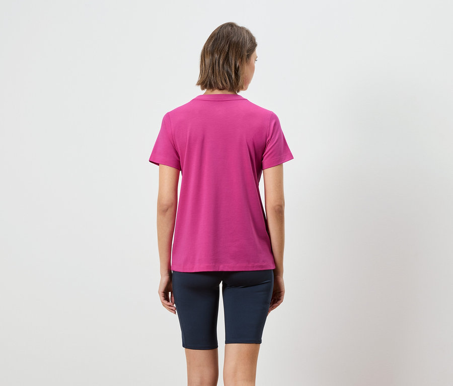 Rückansicht einer Frau mit kurzen braunen Haaren, die ein pinkfarbenes Poloshirt und kurze marineblaue Leggings trägt.