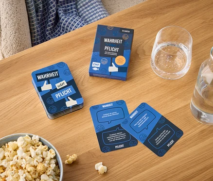Auf einem Holztisch liegen eine Schüssel Popcorn, ein Glas Wasser und eine Packung Spielkarten namens „Wahrheit oder Pflicht“.