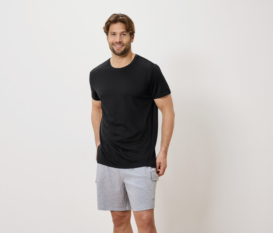Mann mit schwarzem T-Shirt und grauen Shorts vor einem weißen Hintergrund.