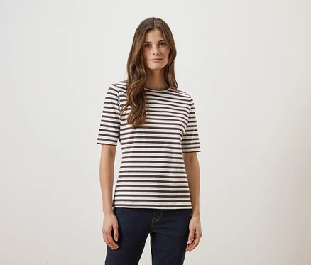 Frau mit langen braunen Haaren, die ein gestreiftes T-Shirt und Jeans vor einem weißen Hintergrund trägt.