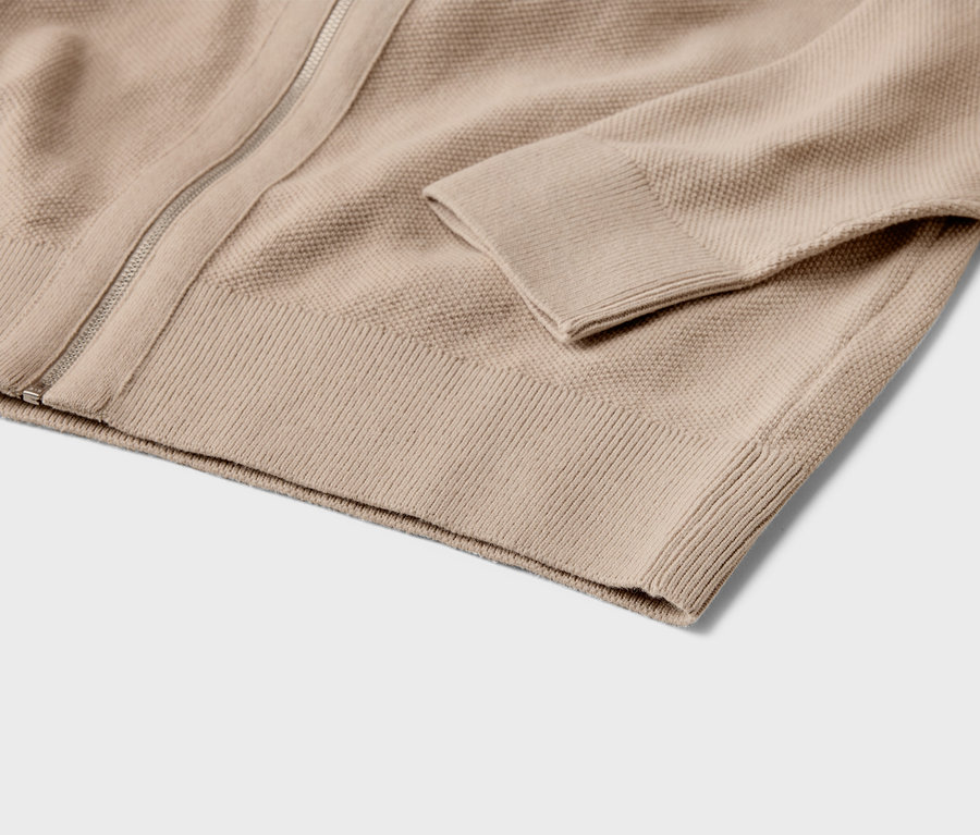 Nahaufnahme einer beigen Strickjacke mit Reißverschluss und Rippbündchen.