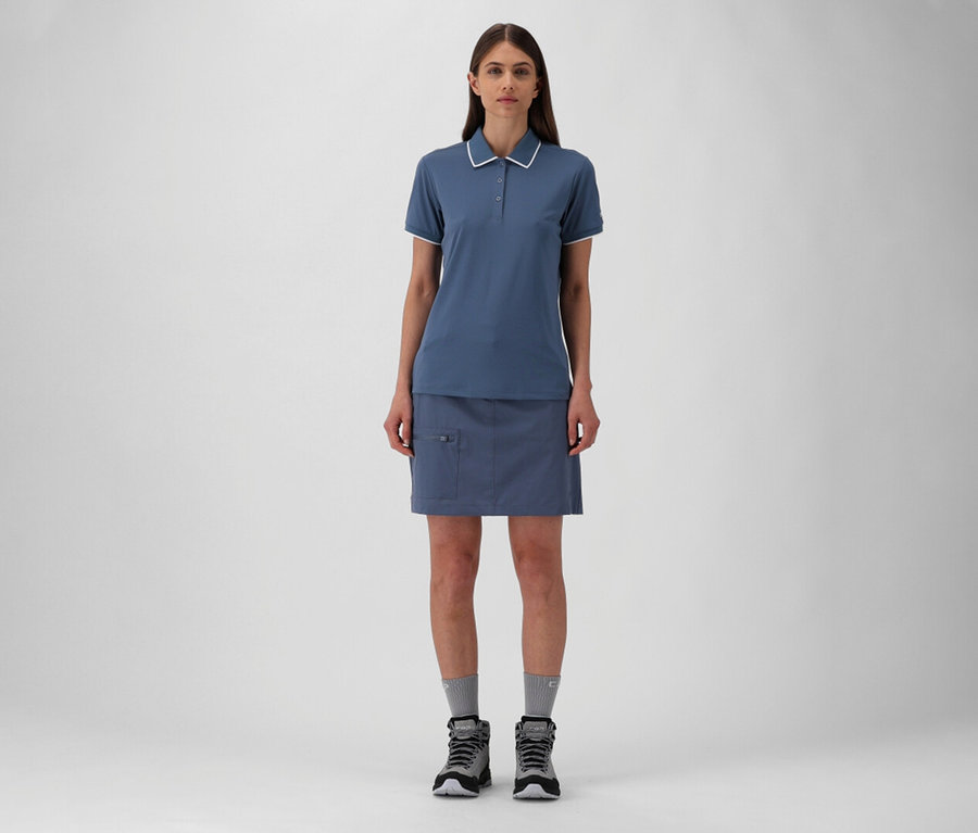 Frau in blauem CMP Damen-Poloshirt aus Stretch-Piqué und Rock mit grauen Socken und Wanderschuhen.