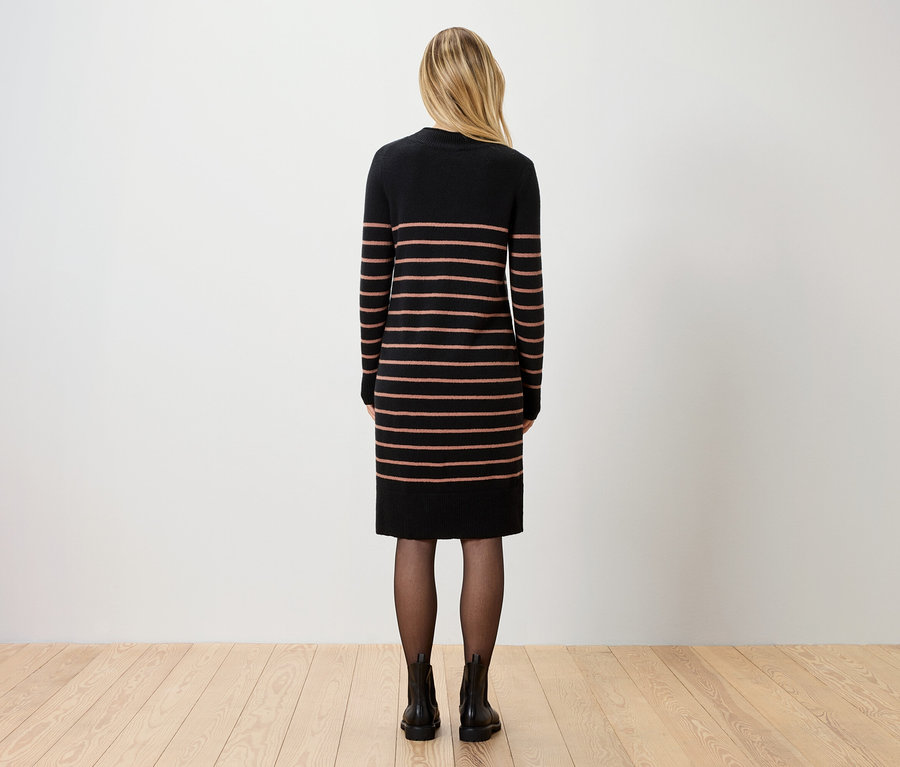 Rückansicht einer Frau mit blonden Haaren, die ein gestreiftes, knielanges Kleid, schwarze Strumpfhosen und Stiefeletten trägt.