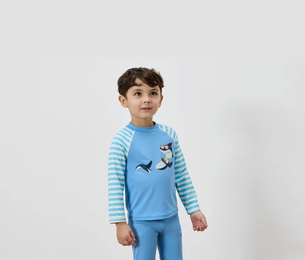 Ein Junge trägt ein hellblaues Langarmshirt mit einem Hai-Design und dazu passende blaue Hosen.