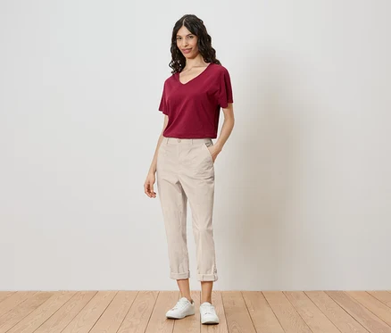 Eine Frau steht vor einer Wand und trägt ein rotes T-Shirt, helle Hosen und weiße Turnschuhe.