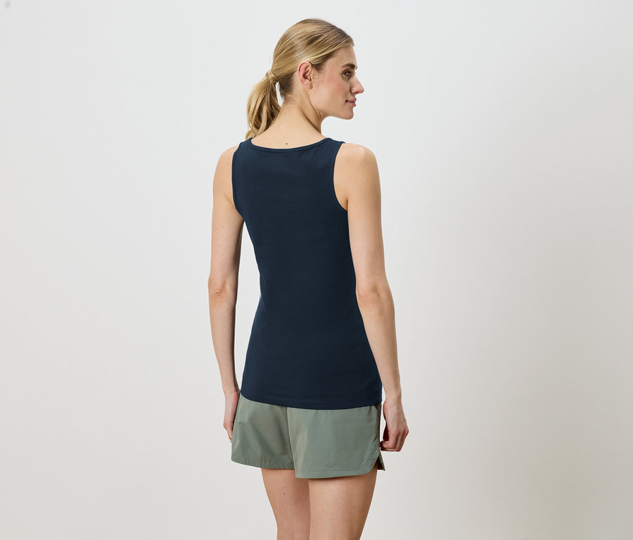 Frau trägt ein ärmelloses, marineblaues Oberteil und grüne Shorts, von hinten gesehen.