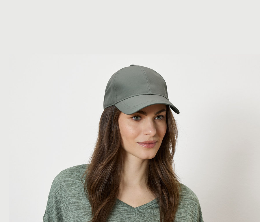 Frau mit grüner Baseballkappe und grünem Oberteil vor einem weißen Hintergrund.