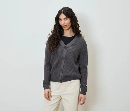 Frau trägt graue Strickjacke mit Knöpfen und helle Hose.