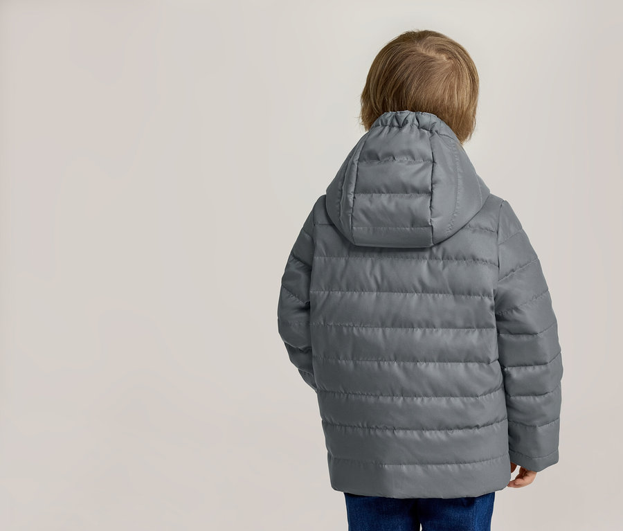 Rückansicht eines Kindes mit blonden Haaren in einer grauen, gesteppten Jacke mit Kapuze und blauen Jeans.