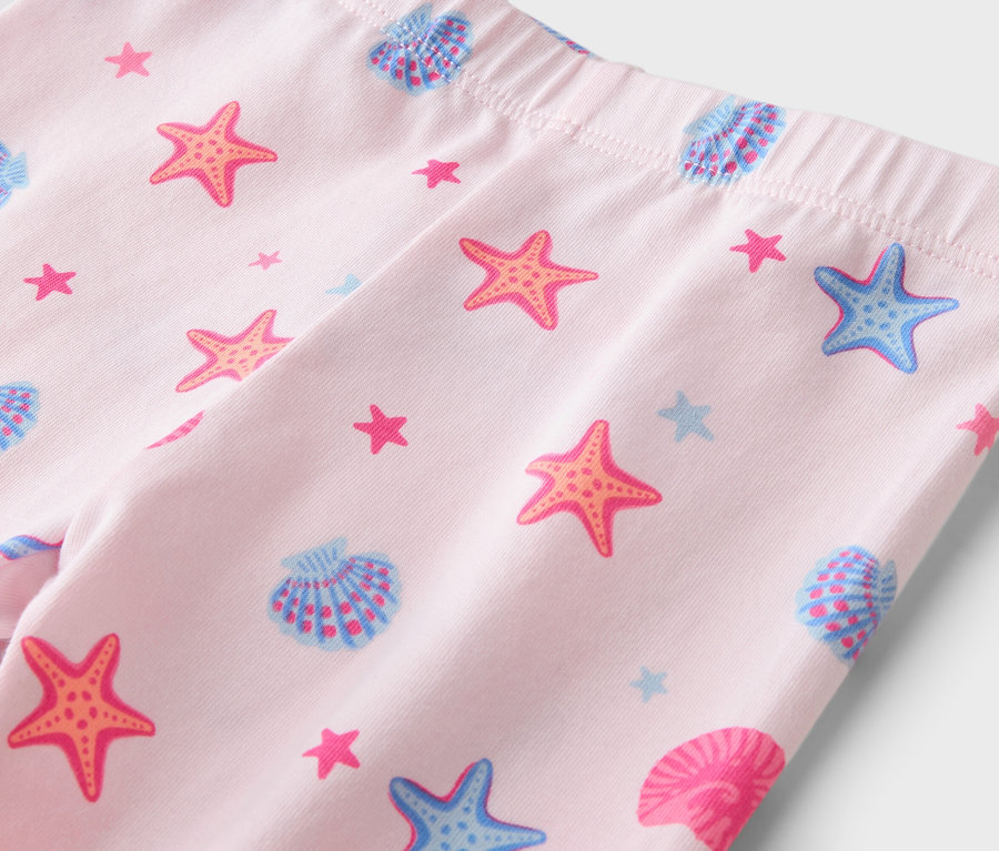 Nahaufnahme von hellrosa Leggings mit Gummibund, bedruckt mit orangefarbenen Seesternen, blauen Seesternen und Muscheln in Blau und Rosa.