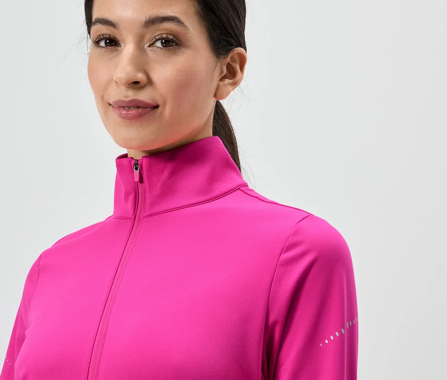 Frau mit Pferdeschwanz trägt eine pinke Jacke mit Reißverschluss und hohem Kragen vor einem weißen Hintergrund.