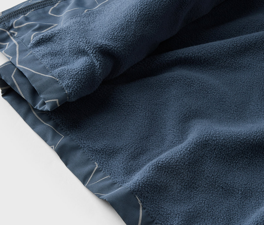 Nahaufnahme einer marineblauen Fleecedecke mit weißem Muster, teilweise zusammengerollt.