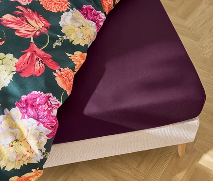 Nahaufnahme eines Bettes mit dunkelviolettem Spannbettlaken und einer Bettdecke mit Blumenmuster.