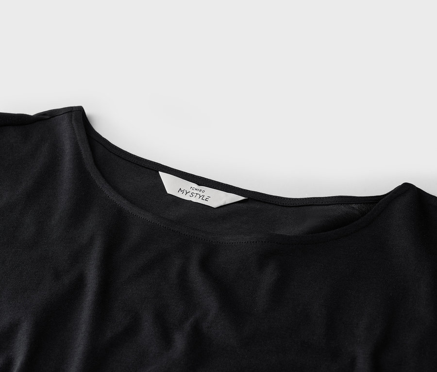 Nahaufnahme eines schwarzen T-Shirts mit einem weißen 'TCHIBO MY STYLE'-Etikett am Kragen.