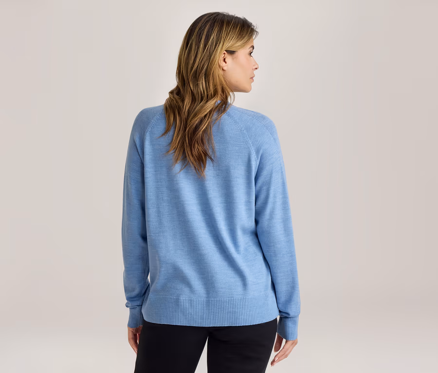 Frau von hinten, trägt einen hellblauen Pullover und schwarze Hose, der Kopf ist leicht zur Seite gedreht.