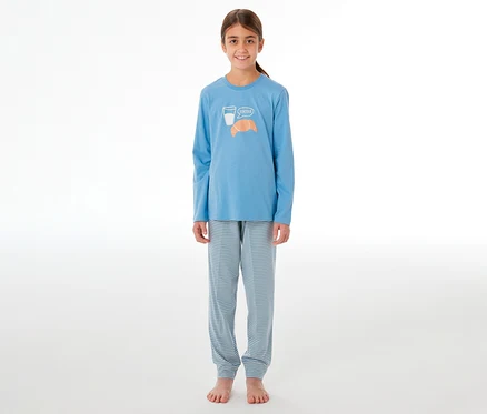 Lächelndes Mädchen in einem SCHIESSER Kinder-Pyjama. Das hellblaue Oberteil hat ein Glas Milch, ein Croissant und "Bonjour" aufgedruckt. Die Hose ist hellblau-weiß gestreift.