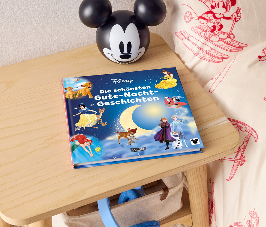 Auf einem Nachttisch liegen ein Disney Gute-Nacht-Geschichtenbuch und eine Mickey-Mouse-Lampe.
