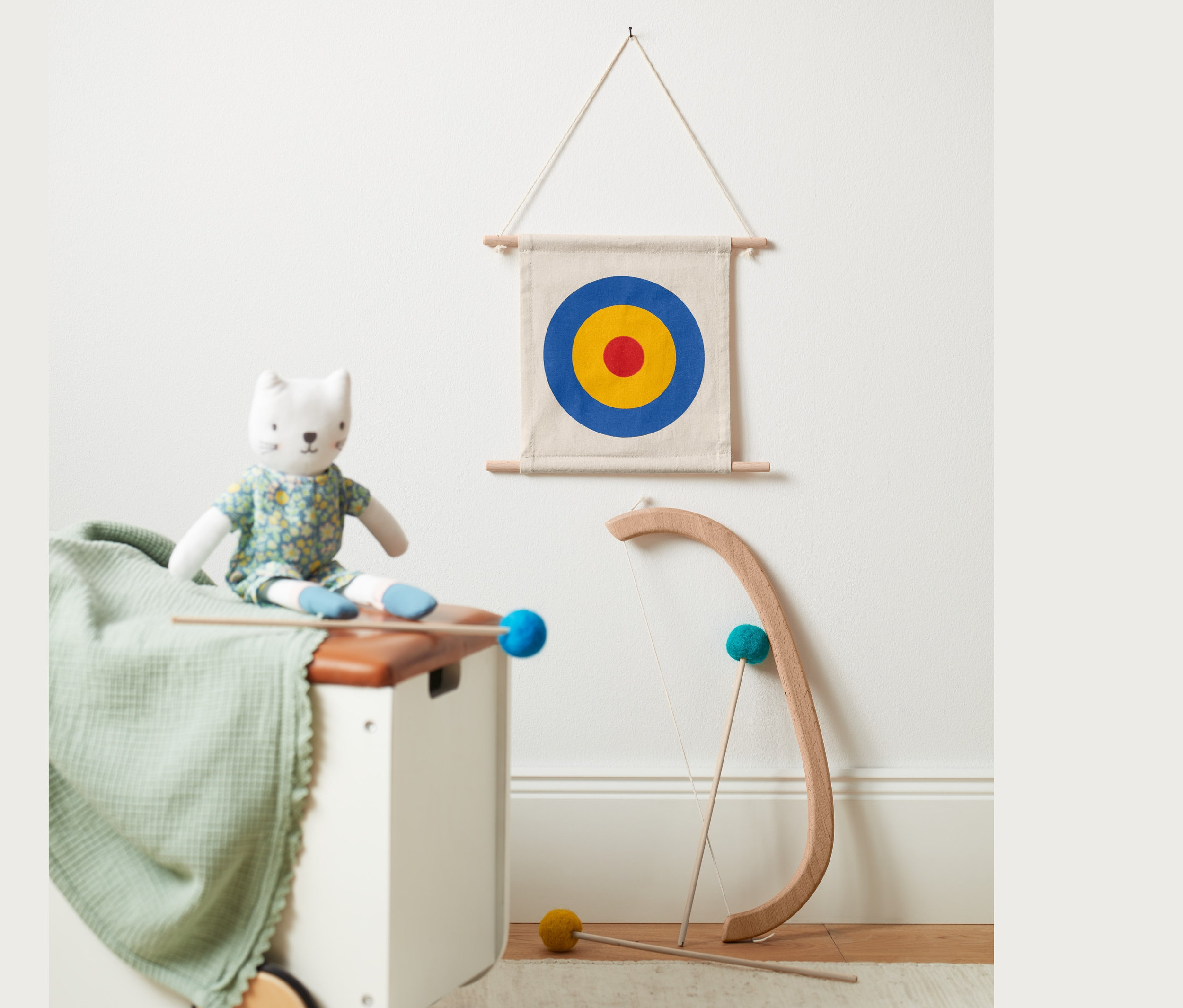 Eine Stoffkatze sitzt auf einer Truhe neben einem Pfeil-und-Bogen-Set und einer Zielscheibe.