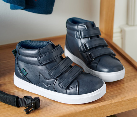 Zwei Sneaker auf einem Holzregal, darunter ein blaues Skateboard.