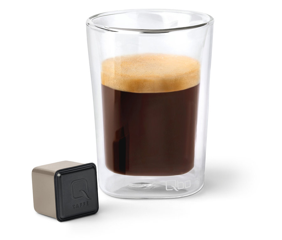 Kaffee in einem transparenten Glas neben einer Qbo Caffè Kapsel.