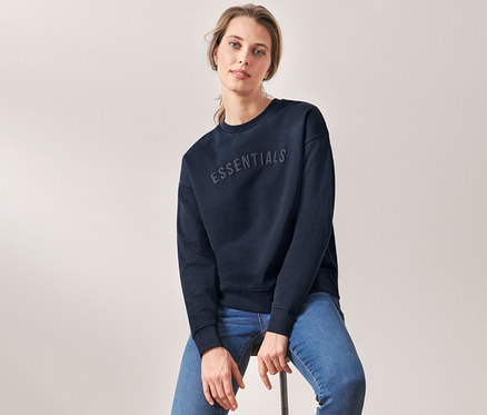 Frau sitzt auf einem Hocker und trägt ein dunkelblaues Sweatshirt.
