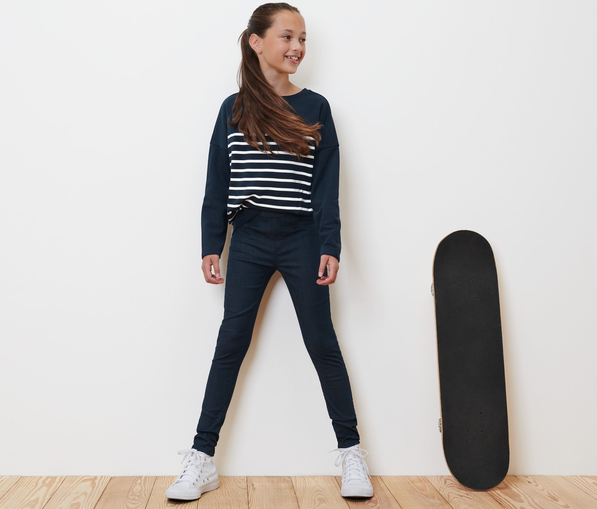 Mädchen steht neben Skateboard und trägt blaue Kinder-Treggings – Fit »Jule«.