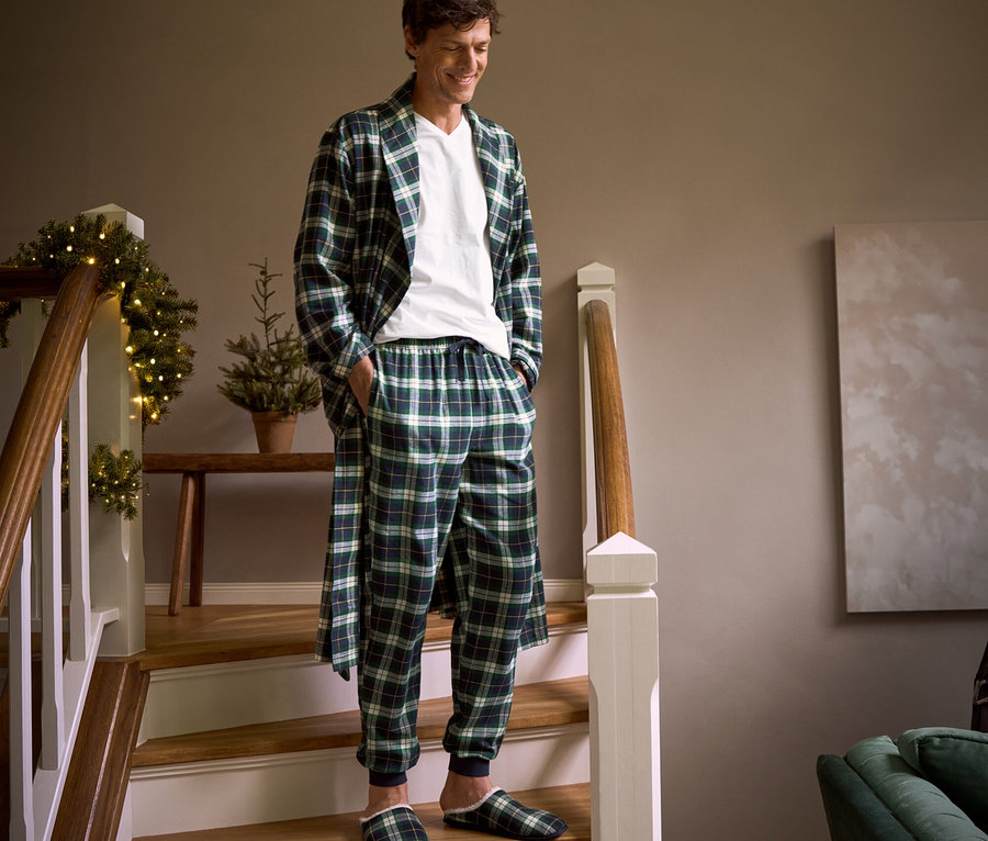 Ein Mann geht eine Treppe hinunter, trägt einen karierten Flanell-Morgenmantel, eine Flanell-Relaxhose, Hausschuhe und 2 T-Shirts mit V-Ausschnitt.