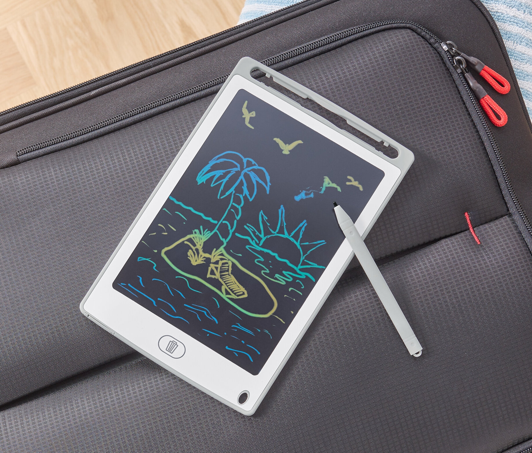 Eine LCD-Schreibtafel mit einer Strandzeichnung liegt auf einem grauen Koffer.