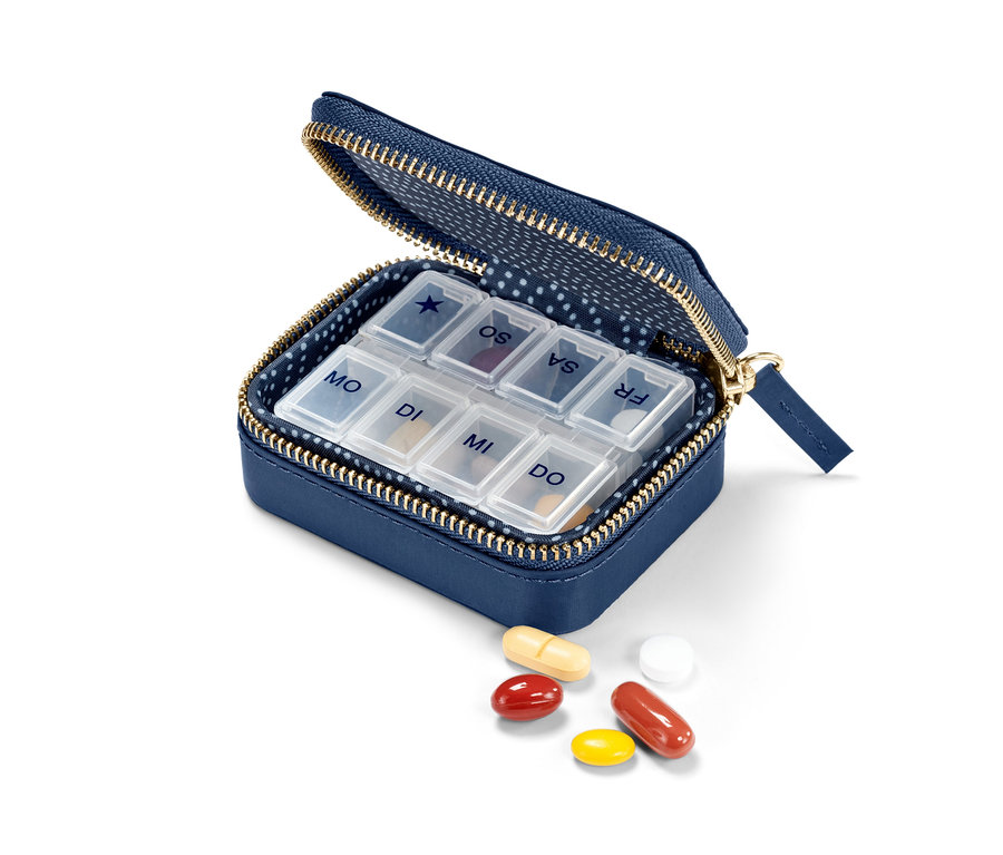 Geöffnete blaue Pillendose mit Hülle und daneben verstreuten Medikamenten.