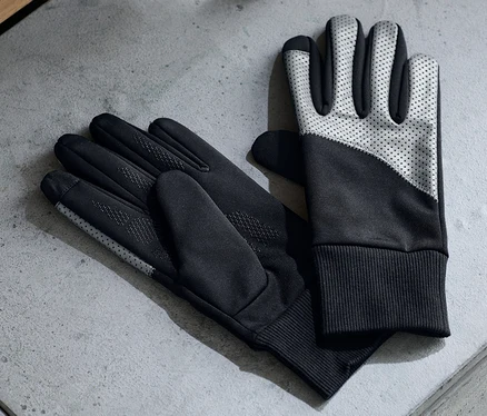 Zwei Paar Windprotection-Handschuhe liegen auf einer grauen Oberfläche neben Ohrhörern und einer Wasserflasche.