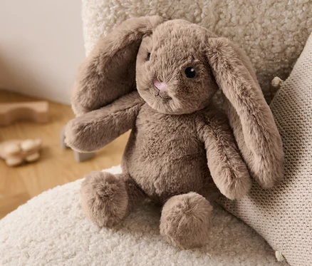 Ein Plüsch-Hase liegt auf einem cremefarbenen Sessel neben einem Kissen.