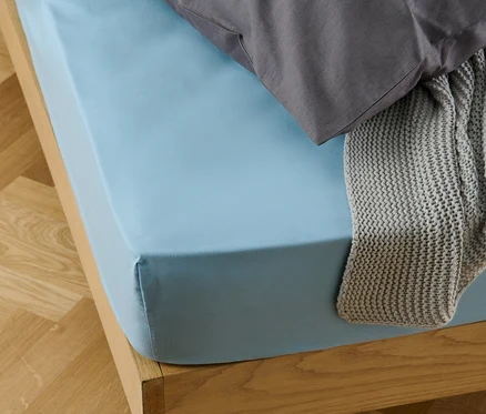 Ein hellblaues Microfaser-Spannbettlaken auf einem Bett mit einem grauen Kissen und einer grauen Strickdecke.