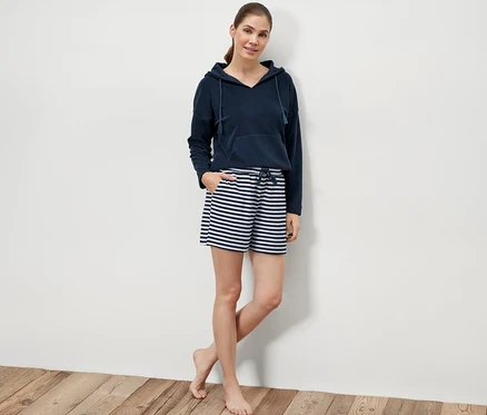 Frau posiert auf Holzboden in Frottee-Shorts und Hoodie.