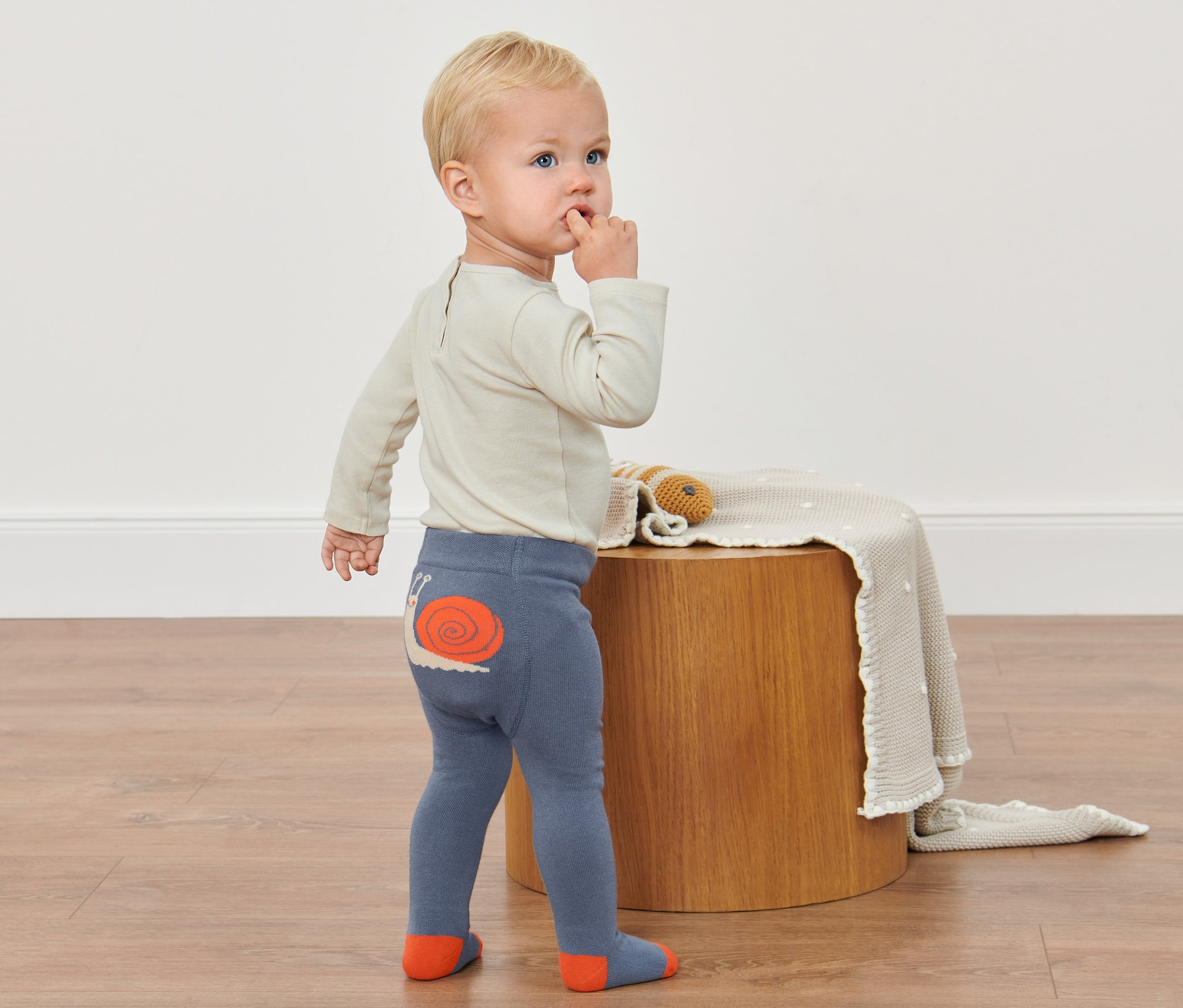 Kleinkind steht auf dem Boden und trägt eine Strumpfhose mit Schneckenmotiv.