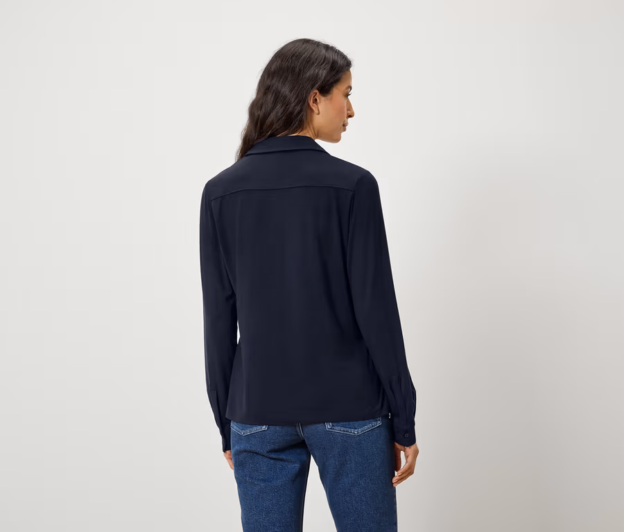 Rückansicht einer Frau mit dunklen Haaren in einem blauen Hemd und Jeans.
