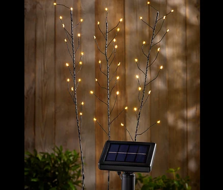 Drei Solar-Spieße mit LED-Lichtern vor einer Holzwand.